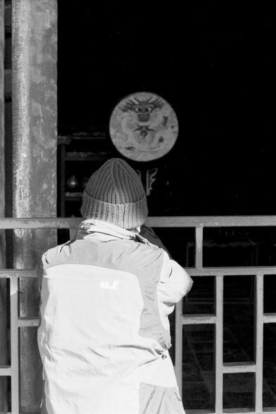 Lucky LUCKY SHD 400 (FF)

##English

A black-and-white photograph of a person standing outdoors, facing a temple or traditional building. The person is wearing a knit hat and a padded jacket. In front of them, a large circular drum with a dragon design is visible through a railing. The scene is dimly lit, and the person appears to be looking at or photographing the drum.

##中文

一张黑白照片，照片中一个人站在户外，面对着一座寺庙或传统建筑。这个人戴着针织帽，穿着羽绒服。前方栏杆内有一个大圆鼓，鼓面上有龙的图案。光线较暗，这个人似乎在观看或拍摄这个鼓。