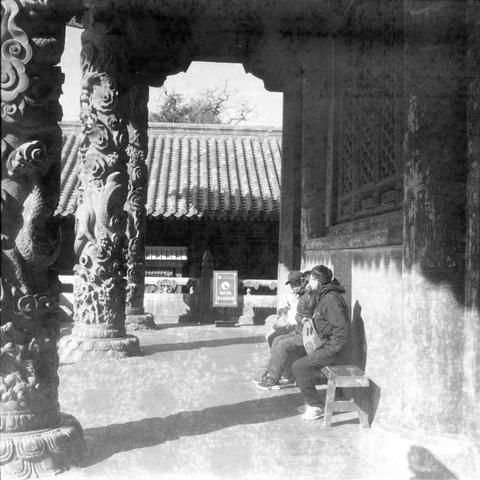 Ilford HP5 Plus 400 (6x6)

English

A black-and-white photograph taken inside a traditional Chinese temple or courtyard. Three individuals are seated on a bench in the foreground, engaged in conversation or looking at something together. The background features intricately carved stone pillars and a traditional tiled roof. A sign with Chinese characters is visible in the background.

中文

一张黑白照片，拍摄于中国传统寺庙或庭院内。前景中有三个人坐在长凳上，似乎在交谈或一起观看某物。背景中有雕刻精美的石柱和传统的瓦片屋顶。背景中还可以看到一个写有汉字的牌子。