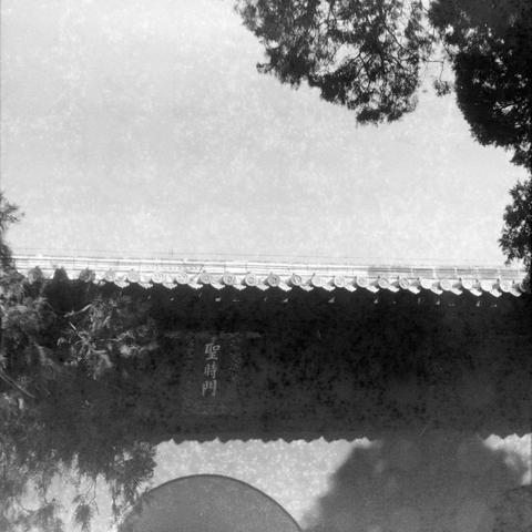 Ilford HP5 Plus 400 (6x6)

English

A black-and-white photograph showing a traditional Chinese architectural structure, likely a wall or gate. The top of the wall features a row of decorative, curved roof tiles typical of Chinese architecture. Trees frame the top left and right corners of the image. On the wall, there are Chinese characters written vertically, which read "聖時門".

中文

一张黑白照片，展示了一座中国传统建筑结构，可能是一面墙或城门。墙顶部有一排装饰性的、弯曲的屋顶瓦片，这是中国建筑的典型特征。照片的左上角和右上角有树木的枝叶。墙上写有汉字“聖時門”，竖排书写。