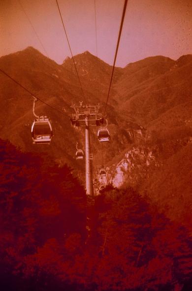 Harman Red 125 (FF) 

English

A vintage-style photograph with a red tint, showing a cable car system. Two cable cars are suspended in the air, moving along cables that stretch across a mountainous landscape. The background features rugged mountains and a forested area. The sky is a light orange hue, adding to the nostalgic and tranquil atmosphere of the scene.

中文

一张带有红色调的复古风格照片，展示了一个缆车系统。两辆缆车悬挂在空中，沿着横跨山区景观的缆索移动。背景是崎岖的山脉和森林区。天空呈现出浅橙色，为场景增添了怀旧和宁静的氛围。