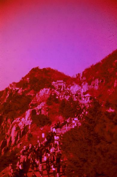 Harman Red 125 (FF)
English
A vintage-style photograph with a strong red tint, showing a mountainous landscape. The scene features a large crowd of people ascending a wide staircase or path that winds up the hillside. The hill is dotted with trees and rocky outcrops. At the top of the hill, there are several buildings, possibly temples or pavilions, with traditional architectural features. The sky is a solid pinkish hue, adding to the nostalgic and surreal atmosphere of the image.
中文
一张带有浓重红色调的…