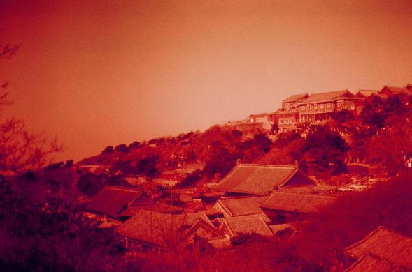 Harman Red 125 (FF)

##English

A sepia-toned photograph featuring a landscape with traditional Chinese architecture. The image shows a cluster of buildings with curved, tiled roofs, likely part of a historical or cultural site. The buildings are nestled among trees on a hillside, with a larger structure visible at the top of the hill. The sky is clear, and the overall atmosphere is serene.

##中文

一张带有棕褐色调的照片，展示了传统中国建筑的风景。图中有一群建筑，屋顶为弯曲的瓦片结构，可能属于某个历史或文化遗址。这些建筑坐落在山坡上的树木之间，山顶上有一个较大的建筑物。天空晴朗，整体氛围宁静。