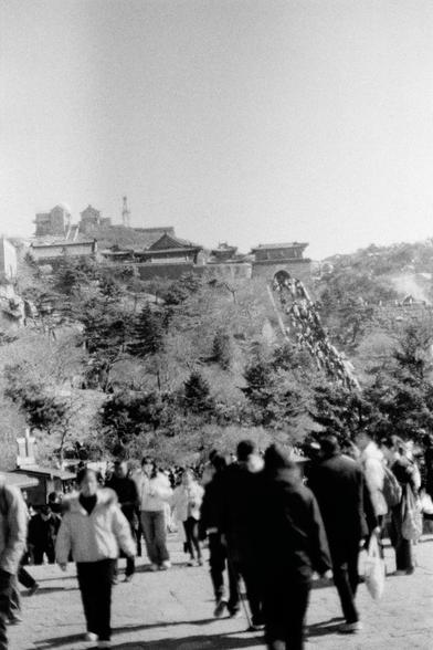 Lucky LUCKY SHD 400 (FF)

English:

A black-and-white photograph showing a crowd of people walking in an open area. In the background, there is a large hill with traditional Chinese architecture, including multi-story buildings with upturned eaves and trees. The scene appears to be a popular tourist spot, with many people walking and some carrying bags.

中文：

一张黑白照片，展示了一群人在开阔区域行走。背景是一座大山丘，山上有传统的中国建筑，包括多层楼房和翘角屋顶，还有树木。场景看起来是一个热门的旅游景点，许多人在行走，有些人拿着袋子。