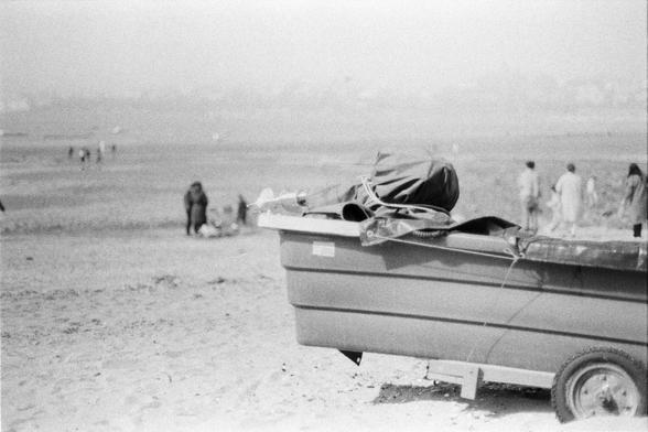Lucky LUCKY SHD 400 (FF)

English

A black-and-white photograph of a sandy or muddy beach with scattered debris and rocks. In the foreground, there is a boat loaded with various items, including what appears to be fabric or tarps. Several people are visible in the background, walking or standing in the open area.

中文

一张黑白照片，拍摄的是一个布满沙子或泥土的海滩，散落着碎石和杂物。前景有一辆装载着各种物品的船，包括看起来像是布料或防水布的东西。背景中有几个人在空地上行走或站立。