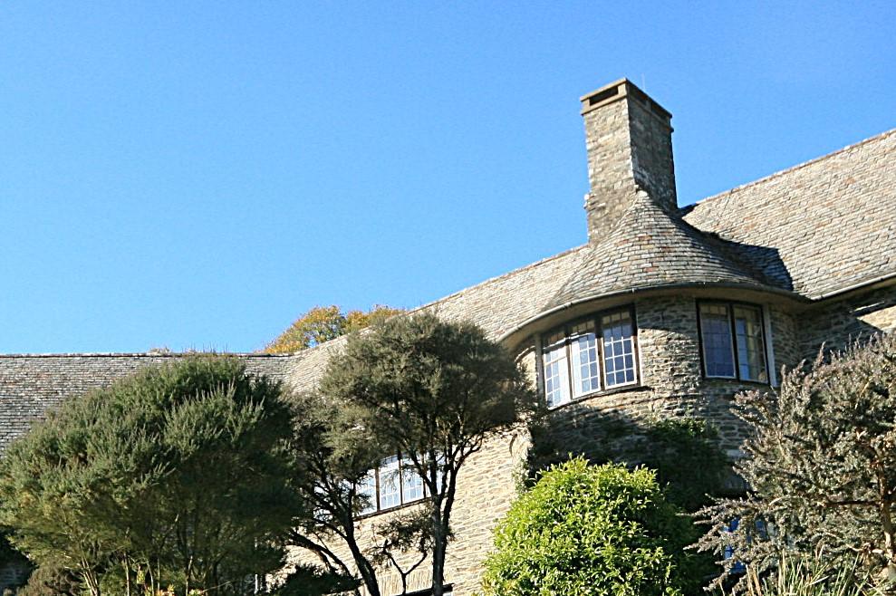 View of the upstairs windows of a stone-built house, with trees in front and blue sky behind.