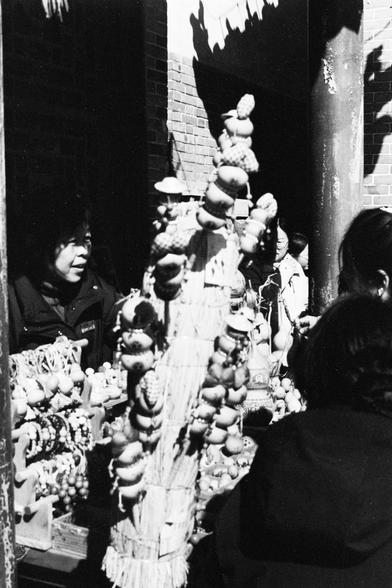 Lucky LUCKY SHD 400 (FF)

English

A black-and-white photo of a street vendor stall. The stall is adorned with various hanging items, possibly dried goods or crafts, stacked in a pyramid shape. Two people are visible: one standing behind the stall and another in the foreground, partially out of frame.

中文

一张黑白照片，展示了一个街边小贩摊位。摊位上悬挂着各种物品，可能是干货或手工艺品，堆叠成金字塔形状。照片中有两个人：一人站在摊位后面，另一人在前景，部分身影未入镜。