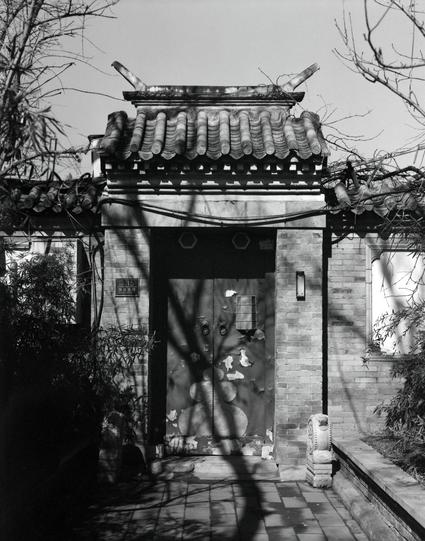 Lucky LUCKY SHD 400 (6x7)

English

A black-and-white photograph of a traditional Chinese building entrance. The entrance features a tiled roof with upturned eaves and a wooden door adorned with decorative metal studs. The door is set within brick walls, and a small sign displaying the number "15" is positioned above the door. Shadows of tree branches are cast across the door and the ground.

中文

一张黑白照片，拍摄的是中国传统建筑的入口。入口处有翘角的瓦屋顶和一扇装饰有金属钉的木门。门两侧是砖墙，门上方有一个写着“15”的小牌子。树枝的影子投射在门和地面上。
