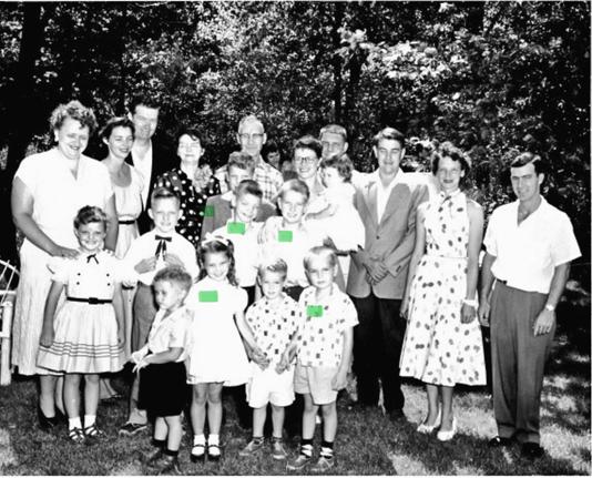 Group family photo of a bunch of 21 white people taken in 1955. There are five individuals with a green bar superimposed on them. They are the only ones alive today. I’m the young boy at center bottom, aged 5yo.