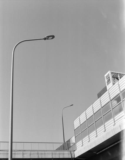 Lucky LUCKY SHD 400 (6x7)

English
A black and white photograph featuring a curved street lamp and a pedestrian overpass. The overpass has a glass and metal structure, and a sign with the letters  visible. The sky is clear, and the overall setting is urban.
中文
一张黑白照片，展示了一盏弯曲的路灯和一个人行天桥。天桥由玻璃和金属结构组成，上面有一个写有英文字样的标志。天空晴朗，整体场景为城市环境。
