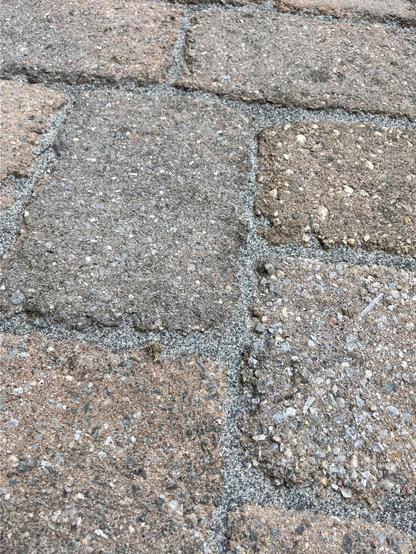 A close-up of a textured stone patio with rectangular tiles in varying shades of brown and gray. Small gaps between are filled with now-cured polymeric sand. 