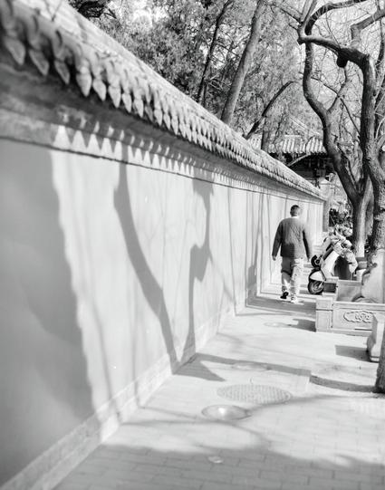 Kentmere PAN 200 (6x7)

English
A black-and-white photograph showing a person walking along a narrow, white-walled corridor. The corridor is lined with traditional Chinese architectural elements, including a tiled roof with decorative eaves. The person is walking away from the camera, and there are trees and a scooter visible in the background.
中文
一张黑白照片，展示一个人沿着一条狭窄的白墙走廊行走。走廊两侧是传统中式建筑元素，包括装饰屋檐的瓦屋顶。此人背对镜头行走，背景中可见树木和一辆摩托车。
