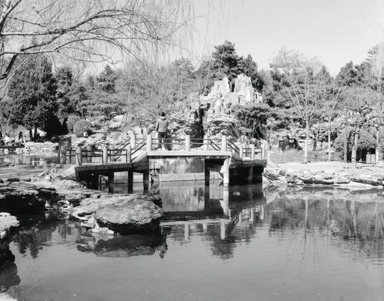 Kentmere PAN 200 (6x7)

##English
Black-and-white photograph of a serene garden scene featuring a stone bridge crossing a narrow waterway. The bridge has traditional railings and is surrounded by rocky landscapes, trees, and shrubs. In the background, a large rock formation rises, adding depth to the tranquil setting.
##中文
一张黑白照片，展示了一个宁静的花园景观，一座石桥横跨在狭窄的水道上。石桥配有传统栏杆，周围是岩石地貌、树木和灌木丛。背景中有一个大型岩石地貌，为宁静的环境增添了深度。
