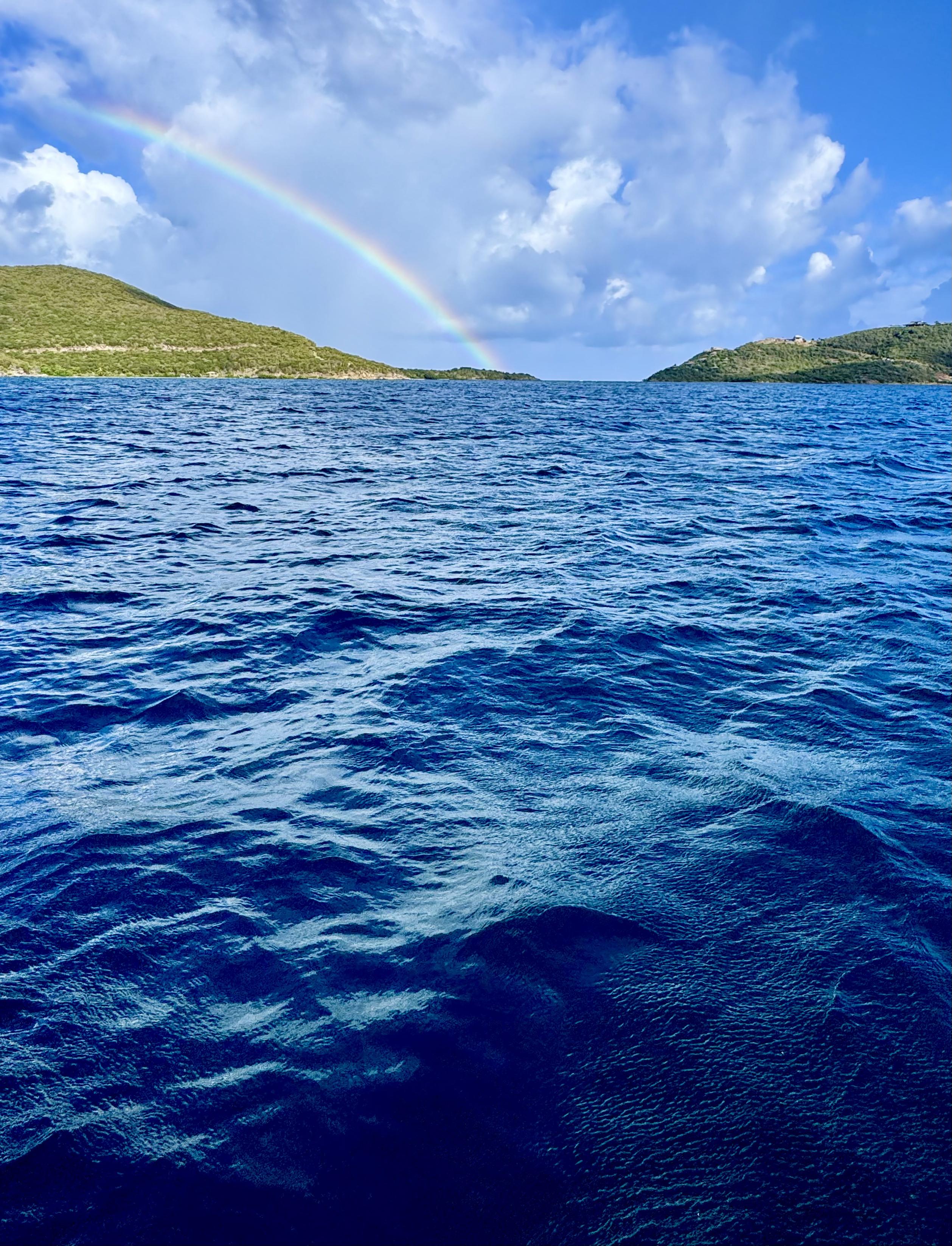 Photo of rainbow over an island. There is a gap in the island and gentle waves in the foreground. Puffy white clouds overhead with some patches of blue.


Leverick Bay, Virgin Gorda, British Virgin Islands.