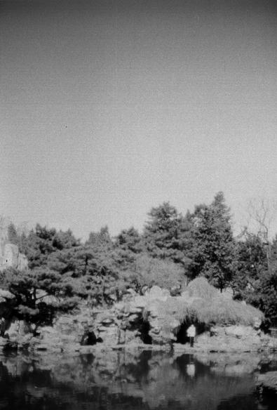 ERA 100 (FF)

English
A black-and-white photograph of a serene garden scene. The foreground features a calm pond reflecting the surrounding landscape. On the far side of the pond, there is a rocky outcrop with various trees and shrubs growing among the rocks. The sky above is clear, adding to the tranquil atmosphere.
中文
一张黑白照片，展现了一个宁静的花园景色。前景是一个平静的池塘，水面倒映着周围的景色。池塘的另一侧是一个岩石突出的地方，岩石间生长着各种树木和灌木。上方的天空晴朗，增添了宁静的氛围。
