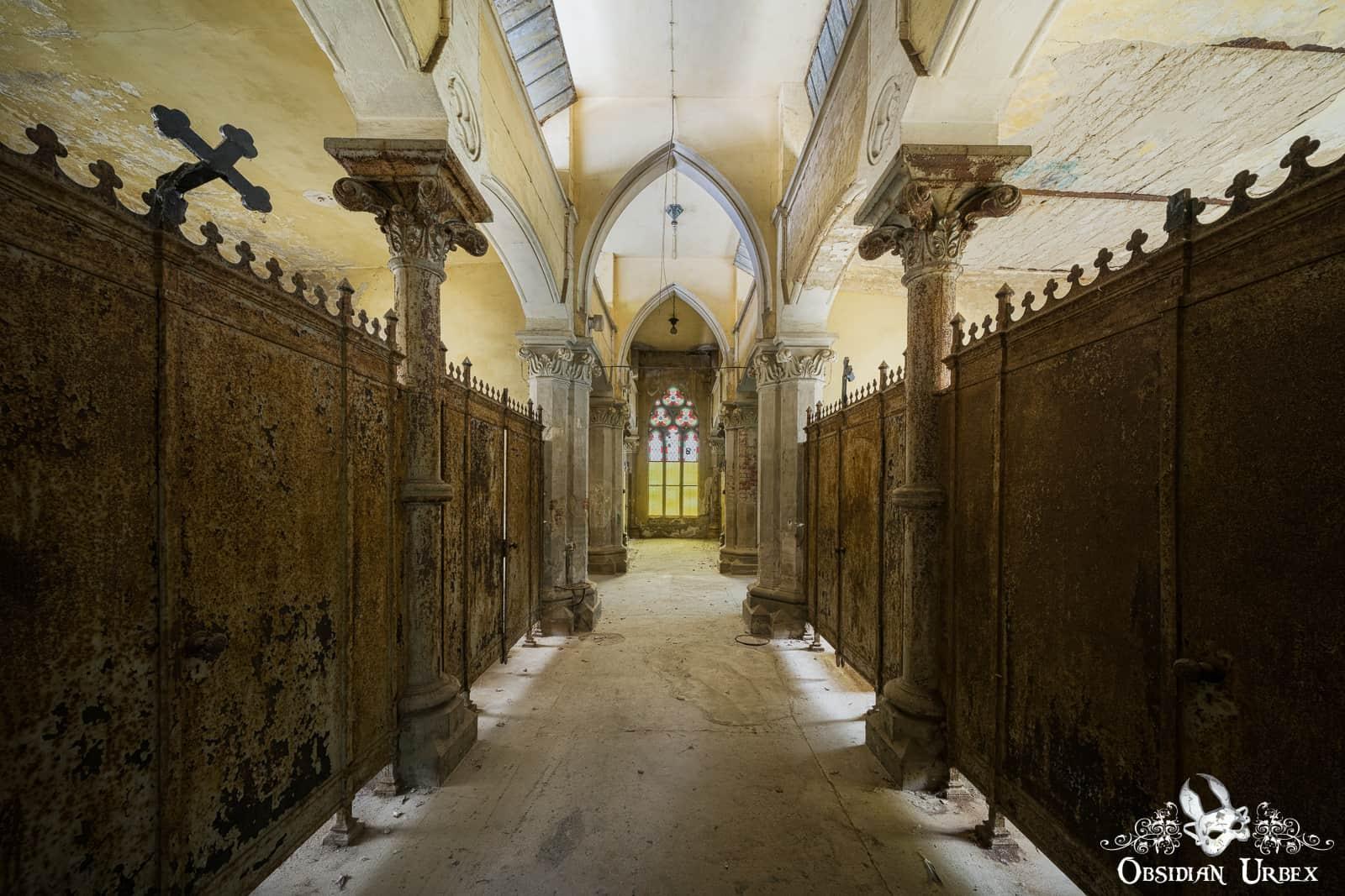 An abandoned German mourning hall features rusty crypts lining a vaulted corridor, leading to a vibrant stained-glass window. A crooked cross is on a left crypt.An abandoned German mourning hall features rusty crypts lining a vaulted corridor, leading to a vibrant stained-glass window. A crooked cross is on a left crypt.