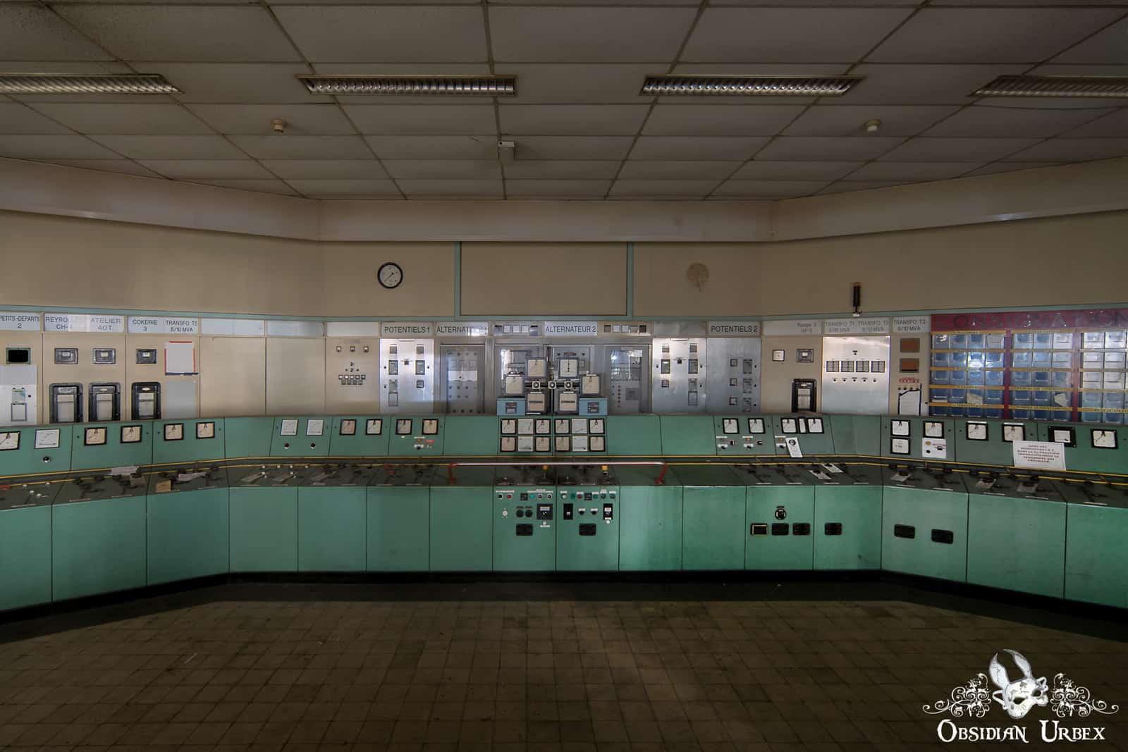 An abandoned power plant control room with a curved mint-green console covered in gauges and switches.