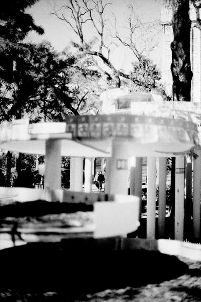 ERA 100 (FF)

English
Black-and-white photograph of a park scene featuring a modern architecture with round, flat platforms. The architecture is partially blurred. In the background, there are more trees and a few people walking, adding a sense of scale and activity to the scene.
中文
黑白照片，展示一个公园场景，其中有一座现代建筑，建筑物有圆形的平台，有些许的模糊。背景中还有更多的树木和几个行走的人，为场景增添了尺度感和活动感。