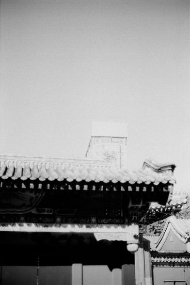 ERA 100 (FF)

English
A black-and-white photograph of the upper section of a traditional East Asian building. The image captures the ornate, curved eaves of the roof, which are layered and intricately designed. In the background, a modern building stands. The sky above is bright and featureless, providing a stark contrast to the dark, detailed roof structure.
中文
一张黑白照片，拍摄的是一座传统东亚建筑的上部。画面展现了屋顶精美的弯曲屋檐，层次分明，设计精细。背景中一栋现代建筑。上方的天空明亮且无特色，与深色、细节丰富的屋顶结构形成鲜明对比。