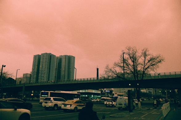 Harman Switch Azure (FF)

English
A cityscape at dusk with a pinkish-orange sky. A busy intersection features multiple lanes of traffic, including cars, buses, and a taxi. An  overpass spans the road, with a few people visible on it. Tall residential buildings rise in the background, and bare trees line the street. The scene is slightly hazy.
中文
黄昏时分的城市景观，天空呈现粉红橙色。繁忙的十字路口有多条车道，车辆包括轿车、公交车和出租车。一座天桥横跨道路，上面有几个人。背景中是高层住宅楼，街道两旁种有光秃秃的树木。整个场景略显朦胧。
