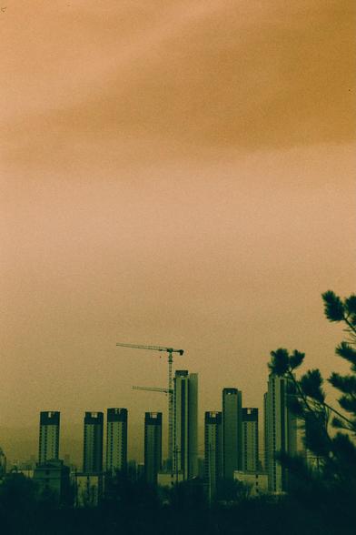Harman Switch Azure (FF)

A city skyline at sunset with a warm orange and yellow gradient sky. Several tall, modern high-rise buildings dominate the horizon, with two construction cranes visible among them. The silhouettes of trees frame the bottom right corner.
##中文
日落时分的城市天际线，天空呈现温暖的橙黄色渐变。地平线上矗立着多栋高大的现代摩天大楼，其中有两台建筑起重机清晰可见。右下角有树木的剪影。