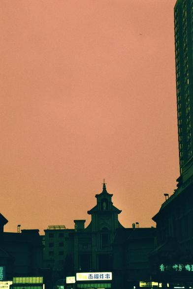 Harman Switch Azure (FF)

##English
A cityscape at dusk with a warm orange sky. The silhouette of a church with a cross on top is visible in the center, surrounded by various buildings. Brightly lit signs in Chinese characters are visible at the bottom, indicating commercial establishments.
##中文
黄昏时分的城市景观，天空呈温暖的橙色。中央可见一座教堂的剪影，顶部有十字架，周围环绕着各种建筑。底部有明亮的中文招牌，显示商业场所。