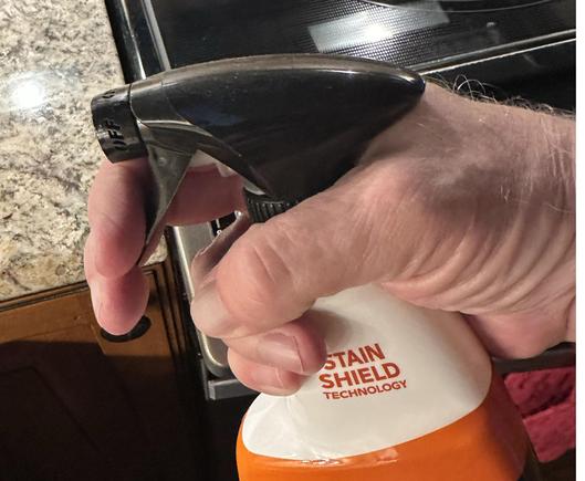 Photo showing a white male hand (my own, in fact) holding a spray bottle of a kitchen cleaner. It’s actually a bad illustration of what I’m trying to show with it, which is how my fingers are curled around the sprayer thingy, and in order for it to work I have to pull my fingers toward my palm. Interestingly, the 1st and 2nd fingers do not hurt, but I can get leverage to pull the thingy without pressing the 4th and 5th fingers against the bottle.