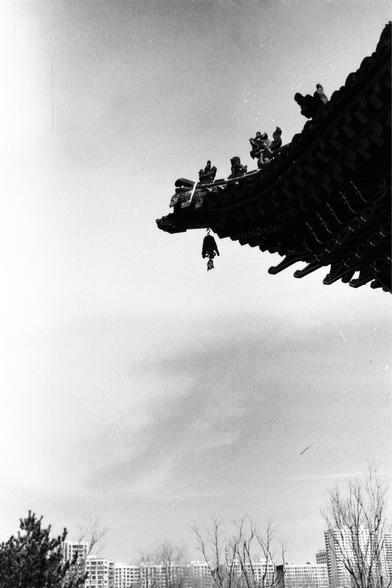 Lucky LUCKY SHD 400 (FF)

##English
Black-and-white photograph capturing the upturned eaves of a traditional Chinese roof. Small figurines are lined up along the ridge of the roof. A bell hangs from the eave. In the background, modern high-rise buildings are visible, contrasting with the traditional architecture.
##中文
黑白照片，拍摄的是一座传统中式建筑的翘起屋檐。屋脊上排列着小雕像。屋檐下悬挂着一个铃铛。背景中可见现代高层建筑，与传统建筑形成对比。