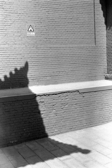 Lucky LUCKY SHD 400 (FF)

##English
Black-and-white photograph of a brick wall with a concrete ledge. A triangular warning sign with Chinese characters "小心坠落" (Beware of Falling) is mounted on the wall above the ledge. The shadow of a tree is cast on the wall and ledge.
##中文
黑白照片，拍摄的是一面砖墙，墙上有一个水泥台面。台面上方的墙上挂有一个三角形警告标志，上面写有汉字“小心坠落”。墙和台面上投射着树的影子。