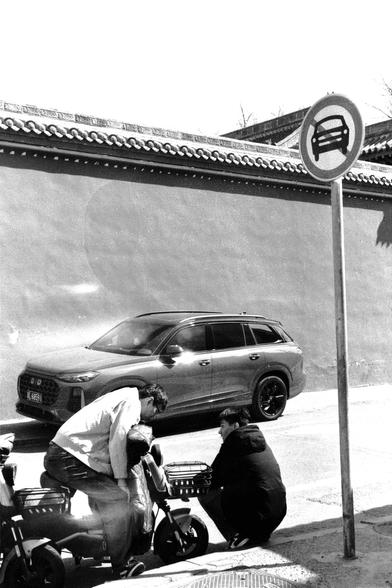 Lucky LUCKY SHD 400 (FF)

##English
Black-and-white photograph of a street scene. A circular traffic sign with a car and a line through it, indicating no parking, is prominently displayed on a pole to the right. In the background, a modern SUV is parked on the street. Two people are near a scooter on the sidewalk, one standing and one crouching. The backdrop includes a traditional tiled roof building.
##中文
黑白照片，展示了一条街道的场景。右侧的杆子上有一个圆形交通标志，上面有一辆车和一条斜线，表示禁止停车。背景中，一辆现代SUV停在街道上。两个人在人行道上靠近一辆摩托车，一人站立，…