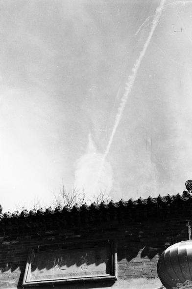 Lucky LUCKY SHD 400 (FF)

##English
A black-and-white photograph showing the upper section of a traditional Chinese building with a tiled roof. The roof features ornate, pointed eaves and a row of small figurines lining the ridge. The sky above is bright, with visible light streaks, possibly from the sun or lens flare. The image captures the architectural details of the roof and the contrast between the dark roof and the bright sky.
##中文
一张黑白照片，展示了中国传统建筑的上部，屋顶为瓦片结构。屋顶的檐角装饰精美，屋脊上排列着一系列小雕像。上方的天空明…