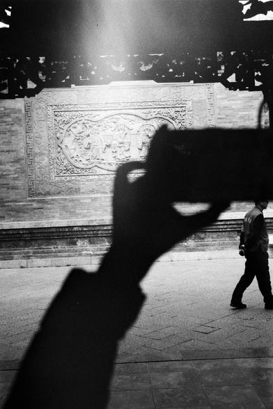 Kentmere PAN 400 (FF)

English
A black-and-white photograph capturing a close-up of a hand holding a camera, silhouetted against a bright light source. In the background, there is a large, intricately carved stone wall with detailed relief sculptures. A person is walking past the wall, slightly blurred due to motion.
中文
一张黑白照片，近距离拍摄了一只手拿着相机的剪影，背景是一个明亮的光源。远处是一面巨大的石墙，上面雕刻着精细的浮雕。有一个人正从石墙前走过，由于运动而略显模糊。
