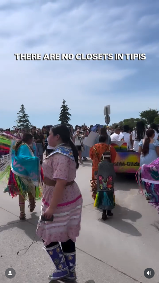 Indigenous people in traditional garb, some with pride-colored fringe on their shawls, are doing a dance in Winnipeg to support the LGBT community. At the top is a slogan that also appears on the T shirts some are wearing: "THERE ARE NO CLOSETS IN TIPIS"