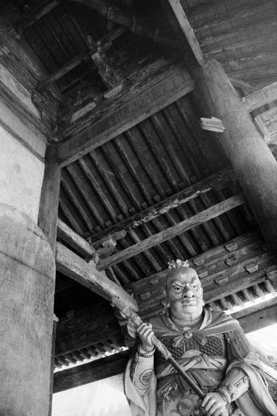 Kentmere PAN 400 (FF)

English
A black-and-white photograph of a statue of a bearded figure in traditional Chinese attire, holding a staff. The statue is positioned under a wooden structure with intricate carvings and a tiled roof. The perspective is from below, looking up at the statue and the roof.
中文
一张黑白照片，展示了一尊身穿传统中国服饰、手持拐杖的胡须人物雕像。雕像位于一个木结构下，该结构有精美的雕刻和瓦片屋顶。视角从下方向上，仰视雕像和屋顶。