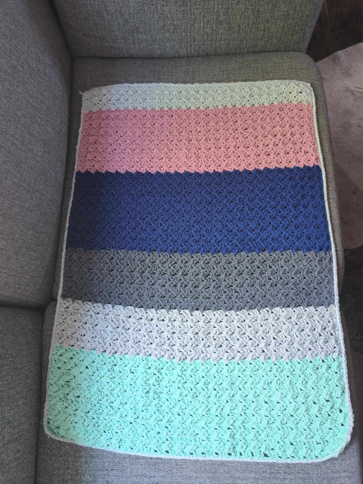 Crochet blanket with light grey, pink, dark blue, darker grey, light grey, and seafoam green