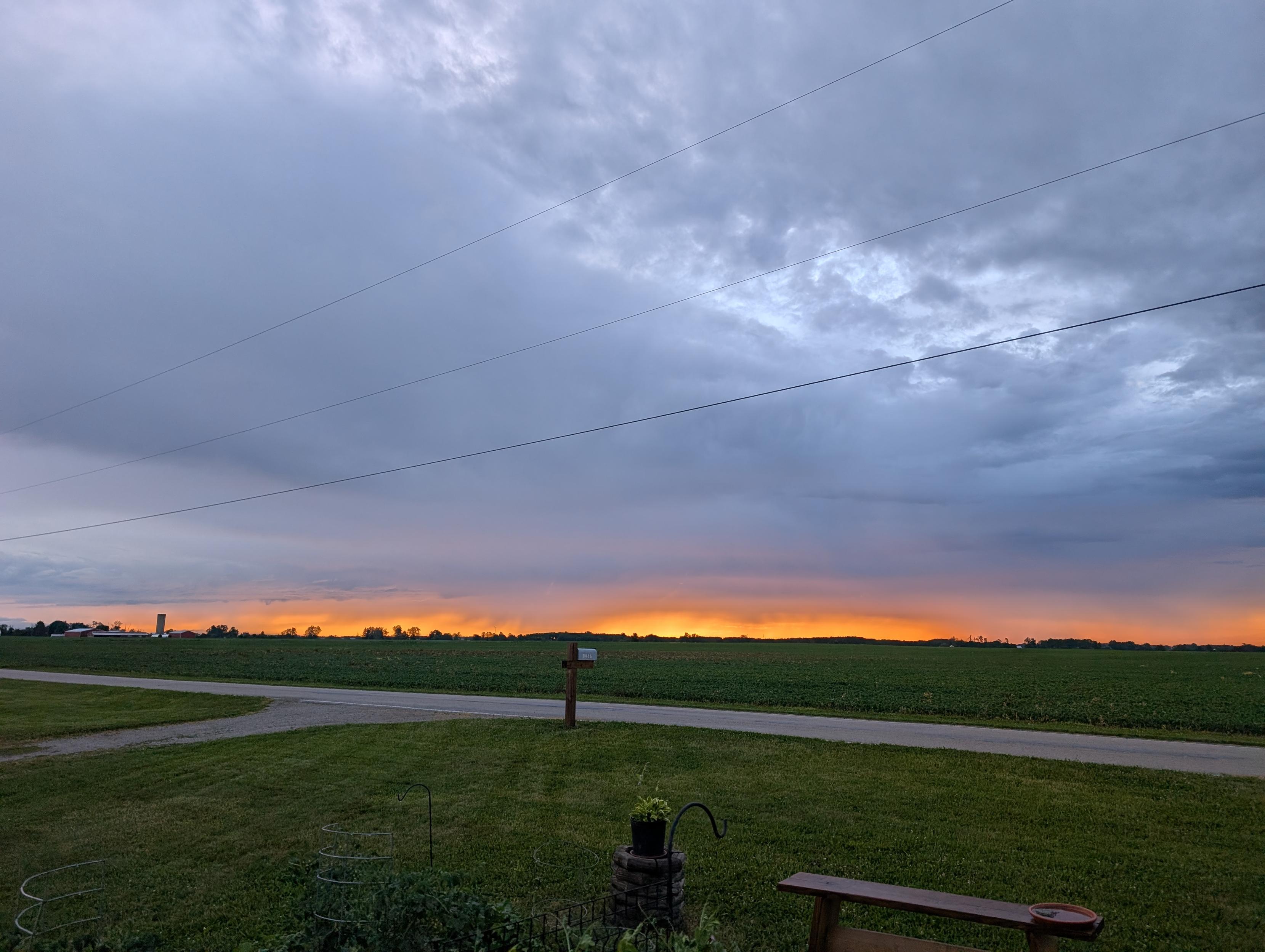 Sunrise over the corn field. Bluish gray clouds swirl and churn across the sky. At the horizon, fuzzy chunks of orange light sneak through the rain, and color a tiny bit of the clouds.