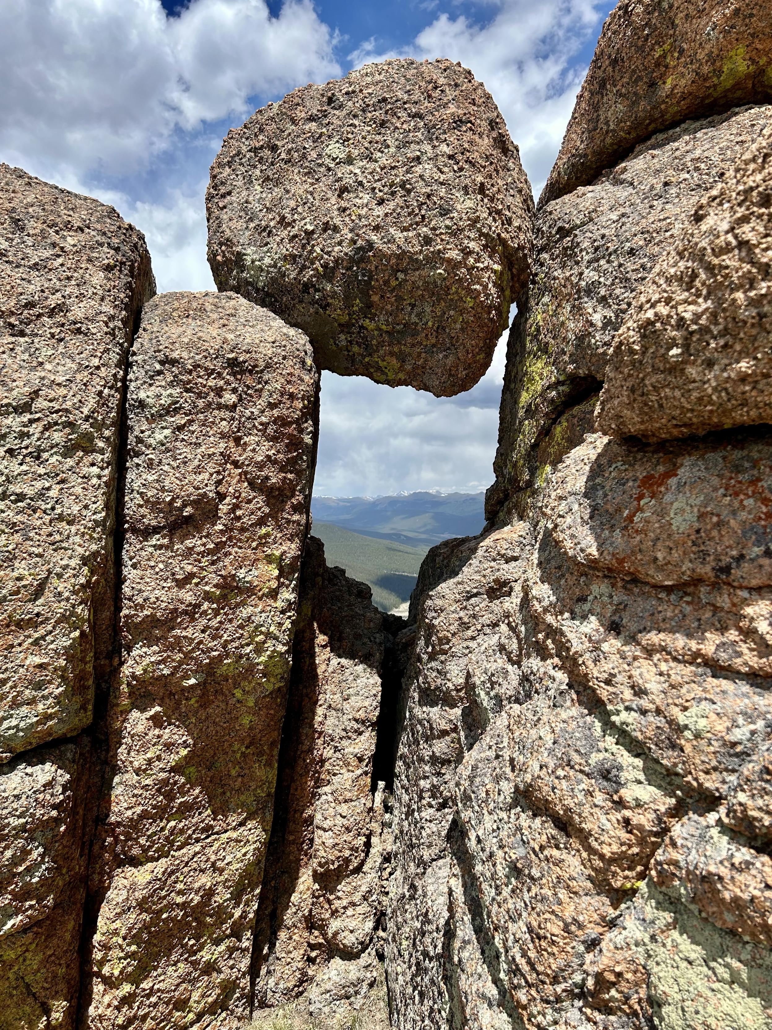 A close-up view of large, textured granite rocks forming a narrow gap, with a cloudy sky and distant mountains in the background.
