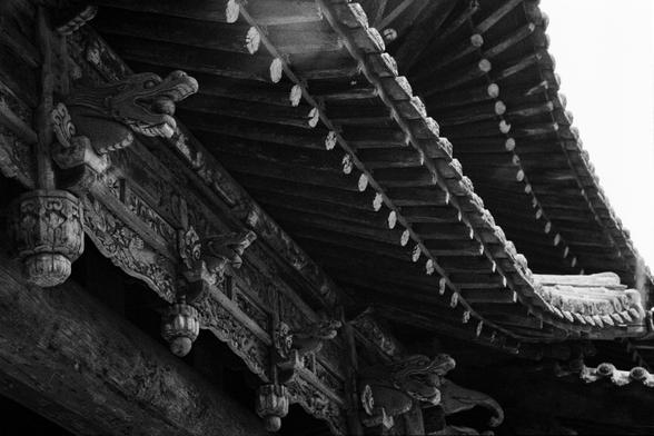 Kentmere PAN 400 (FF)

English
Black-and-white close-up of a traditional Chinese temple roof corner. The image highlights the detailed carvings of mythical creatures and ornamental figures along the eaves. The roof tiles are arranged in a curved, layered pattern, emphasizing the architectural elegance.
中文
黑白特写，拍摄的是传统中式寺庙的屋顶角落。画面突出了屋檐上神话生物和装饰性雕塑的精美细节。屋顶瓦片呈弯曲的层叠排列，强调了建筑的优雅之美。