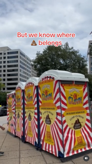 Under a cloudy sky in DC, four port a lets (one handicapped accessible!) are painted with red and white stripes. "END THE GREATEST SHITSHOW ON EARTH: DUMP ON TRUMP!" is written above a poop emoji. On the poop emoji, it says "CRAPPY BIRTHDAY"