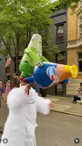 From the account of @lokk_emupp on Ig, the account's owner is a bald white Gen X man wearing a white feather boa over a white T shirt that says "I'm not MAGA white," and he is marching along in a Pride parade with an inflatable green zombie-like figure labeled "EPSTEIN" that is, er, violating an inflatable figure of Trump.