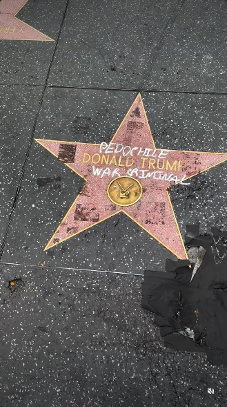 Donald Trump's Hollywood star has "PEDOPHILE" and "WAR CRIMINAL" written over it in white letters. Residue is seen from the protest stickers people put on the star on Sunday, Trump's birthday. In the lower right corner is longstanding damage from where someone trying to jackhammer the star off the Walk of Fame.