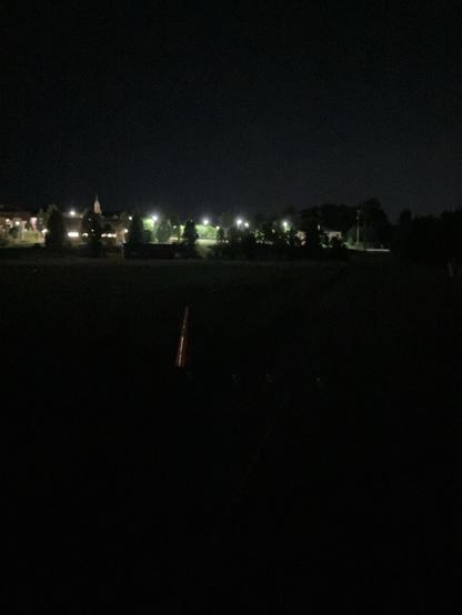 Nighttime view of the middle school track featuring dimly lit buildings and trees, with an orange traffic cone visible in the foreground.