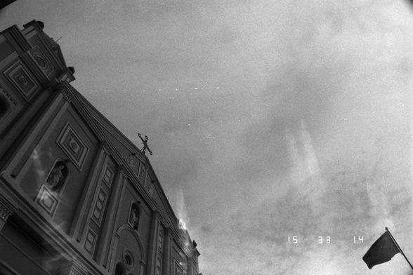 Ilford Pan 400 (FF)

English
Black-and-white photograph of a grand, classical-style church facade. The building features tall columns, arched windows, and decorative niches with statues. A cross is mounted at the peak of the roof, taken from a lower angle. The sky is mostly clear with some clouds. A flag is partially visible on the right side of the image. The timestamp "15 33 14" is visible in the upper right corner.
中文
黑白照片，展示了一座宏伟的古典风格教堂正面。建筑物有高大的柱子、拱形窗户和装饰性壁龛，壁龛内有雕像。十字架位于屋顶的最高处，从较低角度拍摄，天空大部…