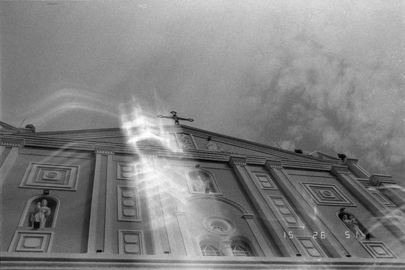 Ilford Pan 400 (FF)

English
Black-and-white photograph of a grand, classical-style church facade. The building features tall columns, arched windows, and decorative niches with statues. A cross is mounted at the peak of the roof. Sunlight creates a strong lens flare effect in the upper center of the image. The timestamp "15 26 51" is visible in the bottom right corner.
中文
黑白照片，展示了一座宏伟的古典风格教堂正面。建筑物有高大的柱子、拱形窗户和装饰性壁龛，壁龛内有雕像。十字架位于屋顶的最高处。阳光在图像上方中央形成强烈的镜头光晕效果。右下角可见时间戳“15 26 51”。