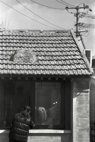Ilford FP4 Plus 125 (FF)

English
A black-and-white photograph of a tiled roof with a bird's nest placed on top. The roof tiles are arranged in a traditional pattern, and the nest is made of twigs and other natural materials. In the background, there is a utility pole with electrical wires and an air conditioning unit attached to the wall below the roof. A person in a dark jacket is partially visible at the bottom left of the image.
中文
一张黑白照片，展示了一个铺有瓦片的屋顶，上面放着一个鸟巢。屋顶的瓦片排列成传统图案，鸟巢由树枝和其他天然材料制成。背景…