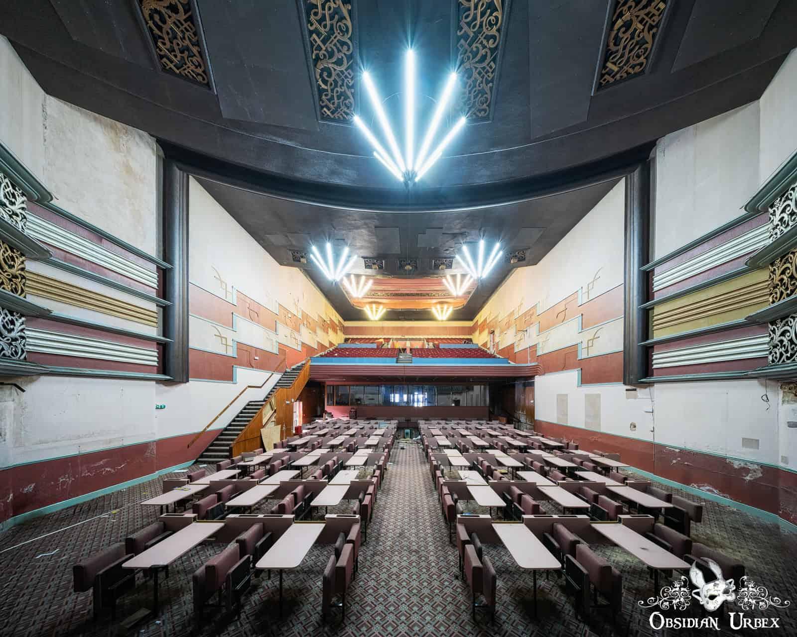 An abandoned Art Deco cinema, with rows of tables and chairs filling the grand hall leading to a stage