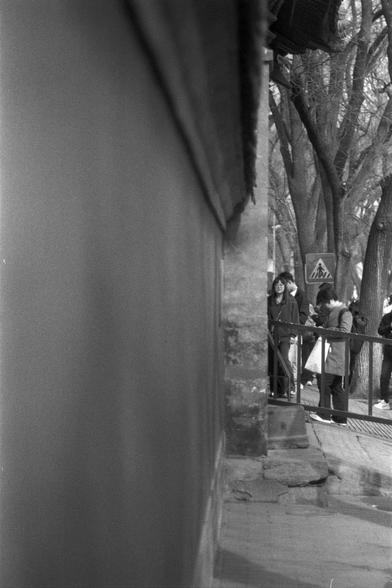 Ilford FP4 Plus 125 (FF)

English
A black-and-white photograph showing a group of people standing near a railing, possibly on a bridge or walkway. The scene includes bare trees in the background and a triangular pedestrian warning sign. The image is taken from the side, with a wall visible.
中文
一张黑白照片，拍摄的是一群人站在栏杆附近，可能是在桥或步道上。背景中有光秃秃的树木，还有一个三角形的行人警告标志。照片从侧边拍摄，左侧可见墙壁。