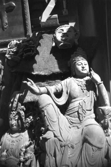 Ilford FP4 Plus 125 (FF)

##English
Black-and-white photograph of a detailed stone carving depicting multiple Buddhist figures. The central figure is a seated Buddha with an elaborate headdress and flowing robes, gesturing with both hands. Surrounding the Buddha are smaller figures, also intricately carved, with distinct facial features and traditional attire. The carving appears to be part of a larger structure or wall.
##中文
黑白照片，展示一个详细的石雕，描绘了多个佛教人物形象。中央是一尊坐佛，头戴精美头饰，身披流动的袈裟，双手做手势。佛陀周围是一些较小的人物形…
