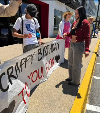 The Palo Alto Raging Grannies and other protesters are out at an anti-Elon Musk protest with a banner that says "CRAPPY BIRTHDAY TO YOU ELON." They marched through the Stanford shopping center as they do every week, but with even more verve.