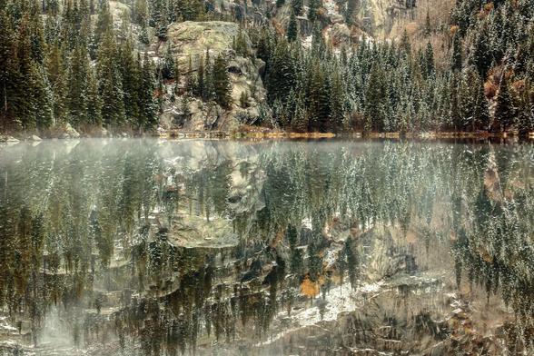 Bear lake

Photo at Bear Lake in Rocky Mountain National Park. The water is absolutely still, reflecting the opposite shore like a mirror. The water line extends across the image just above the center. Pine trees grow down to the edge. A footpath can be seen above the water as a streak of light brown. There is a wooden bridge at center left. There is a light coating of snow in the trees and on rocks above them. At the bottom of the image more snow can be seen reflected in the water. A shallow l…