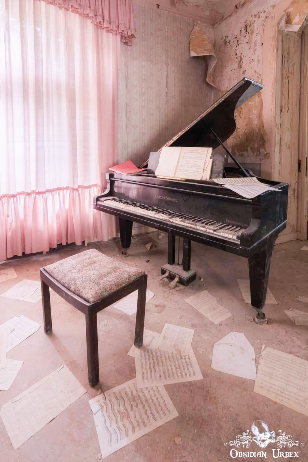 An abandoned room features a black Chapman Instruments grand piano, stool, and scattered sheet music on the floor. Pink curtains and peeling walls show decay.